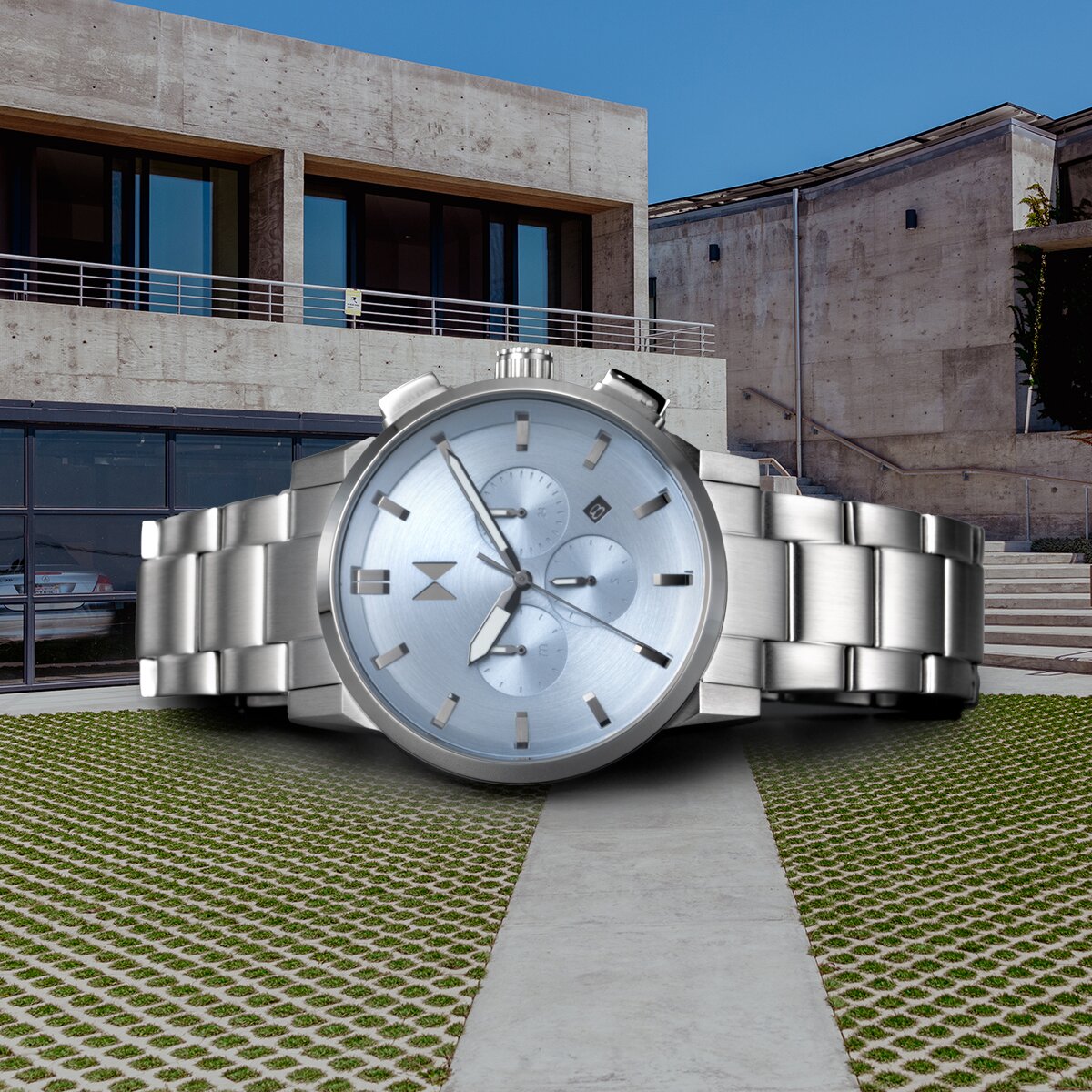 Chrono II watch with stainless steel bracelet and blue chronograph dial laying on it's side in front of a house.