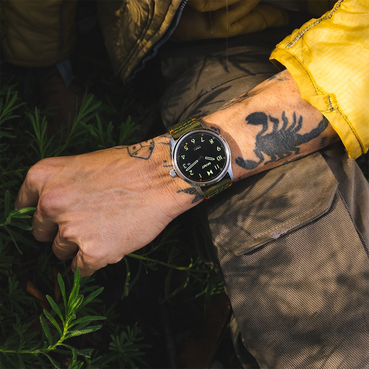 Man with tattoos and yellow jacket wearing the Field II solar watch with green strap.