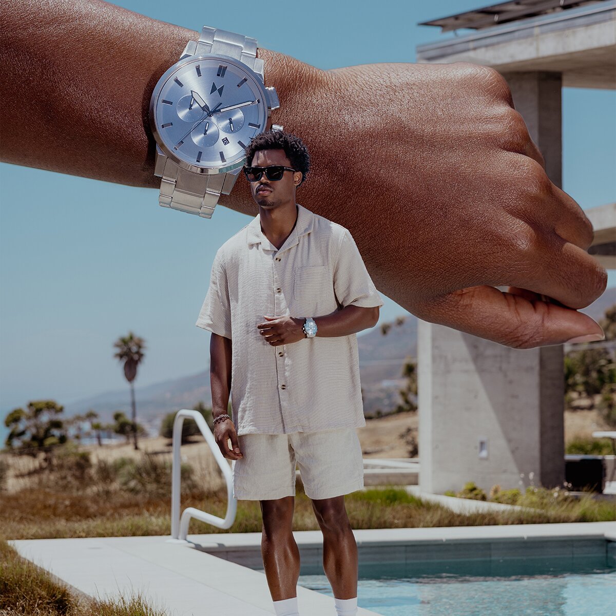 Man by a pool in a tan linen set wearing the Chrono II watch with stainless steel bracelet and blue chronograph dial.