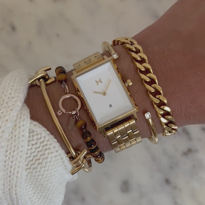 Rectangular gold-tone watch with a white dial worn among layered gold bracelets as the wrist moves gently.